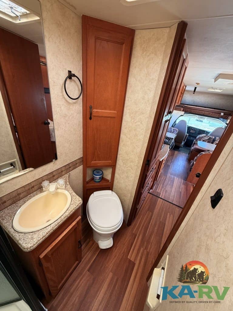 RV bathroom with wooden cabinets, toilet, and small sink in a 2013 Coachmen Freelander 23CB.