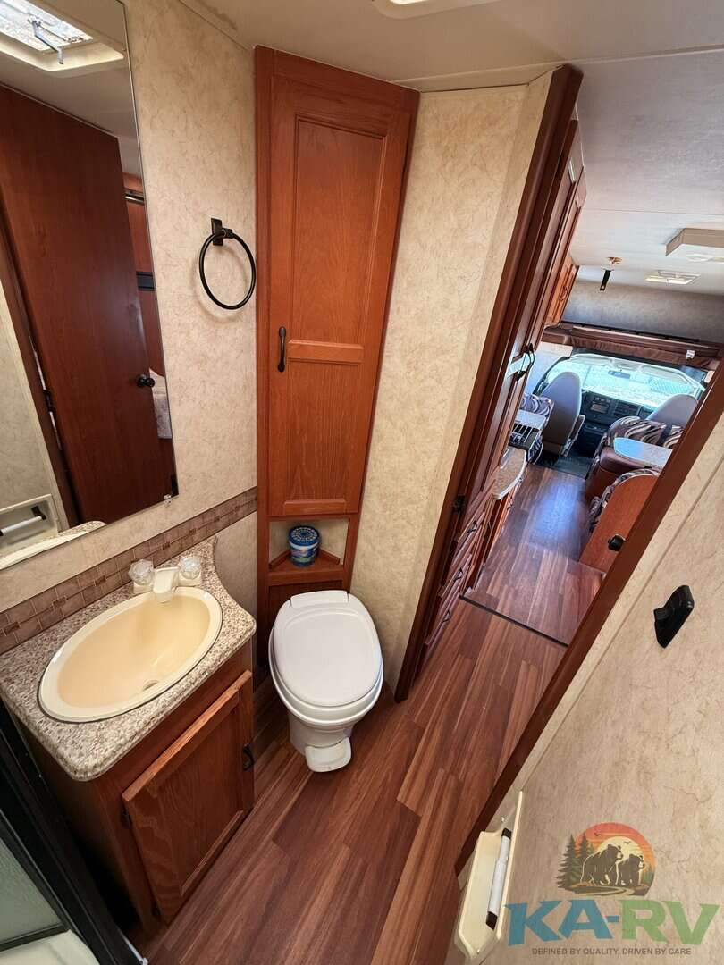 RV bathroom with wooden cabinets, toilet, and small sink in a 2013 Coachmen Freelander 23CB.
