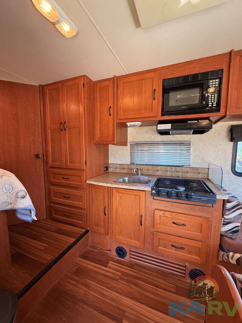 Compact RV kitchen with wooden cabinets, microwave, stove, and sink for optimal space utilization.