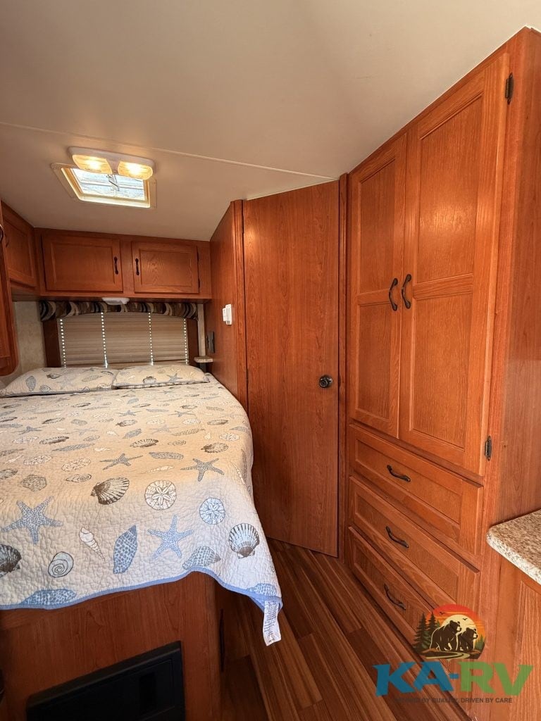 Interior view of a cozy RV bedroom with wooden cabinets and a bed with ocean-themed bedding.