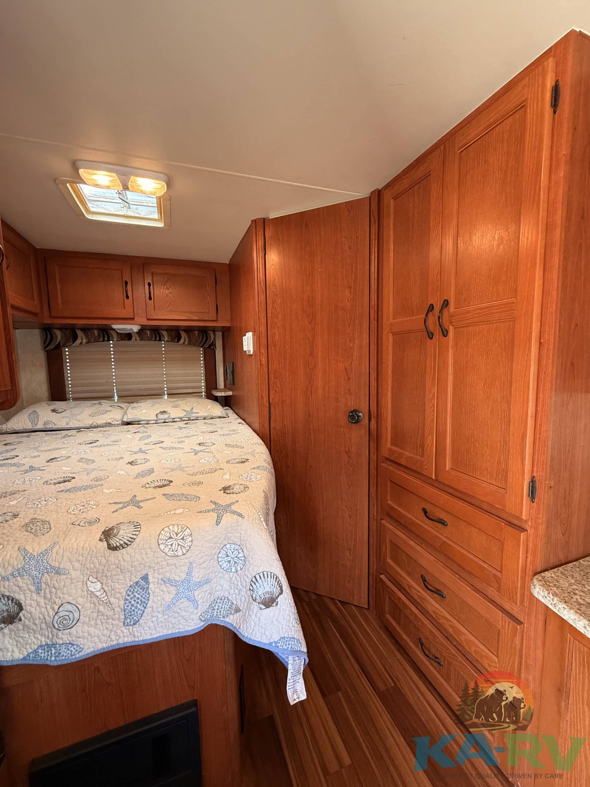 Interior view of a cozy RV bedroom with wooden cabinets and a bed with ocean-themed bedding.