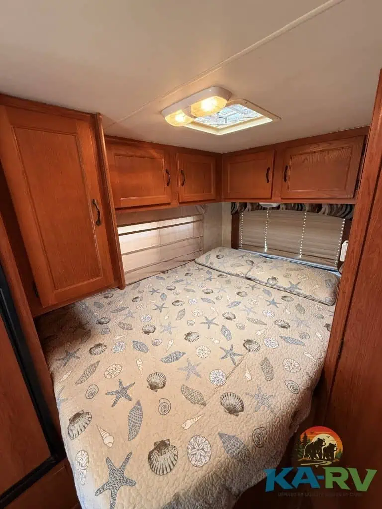 Cozy RV bedroom with wooden cabinets and starfish-themed bedding.