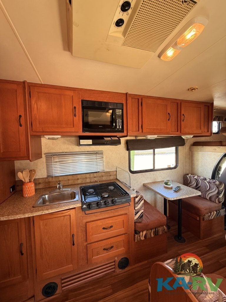 RV kitchen with wooden cabinets, microwave, stove, and small dining area.