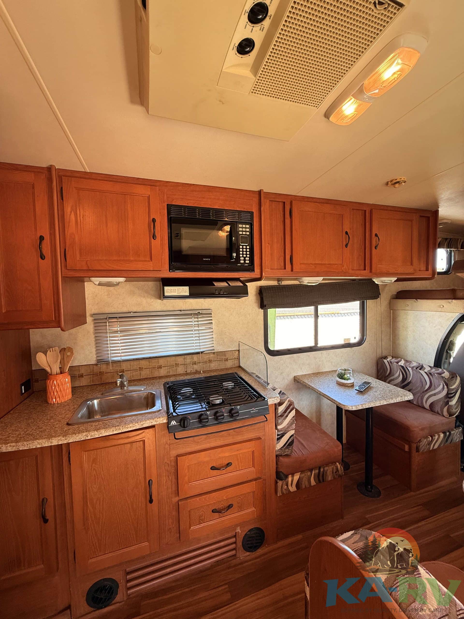 RV kitchen with wooden cabinets, microwave, stove, and small dining area.