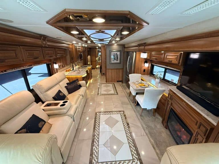 Luxury RV interior with leather sofas, dining area, and entertainment center.