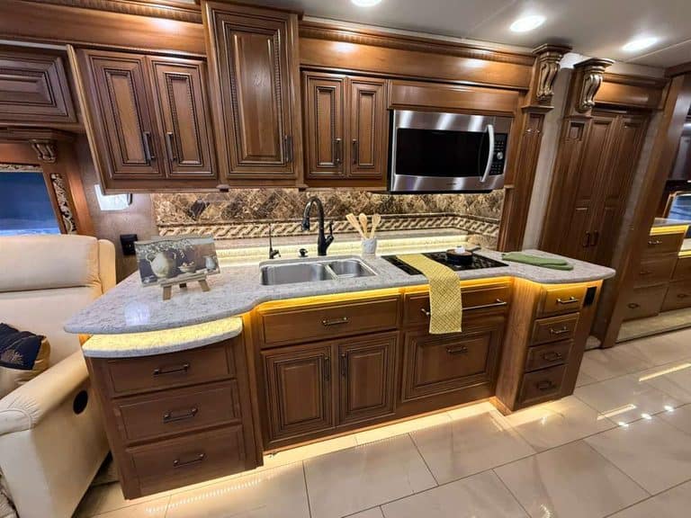 Elegant RV kitchen with wooden cabinets, granite countertops, and modern appliances.