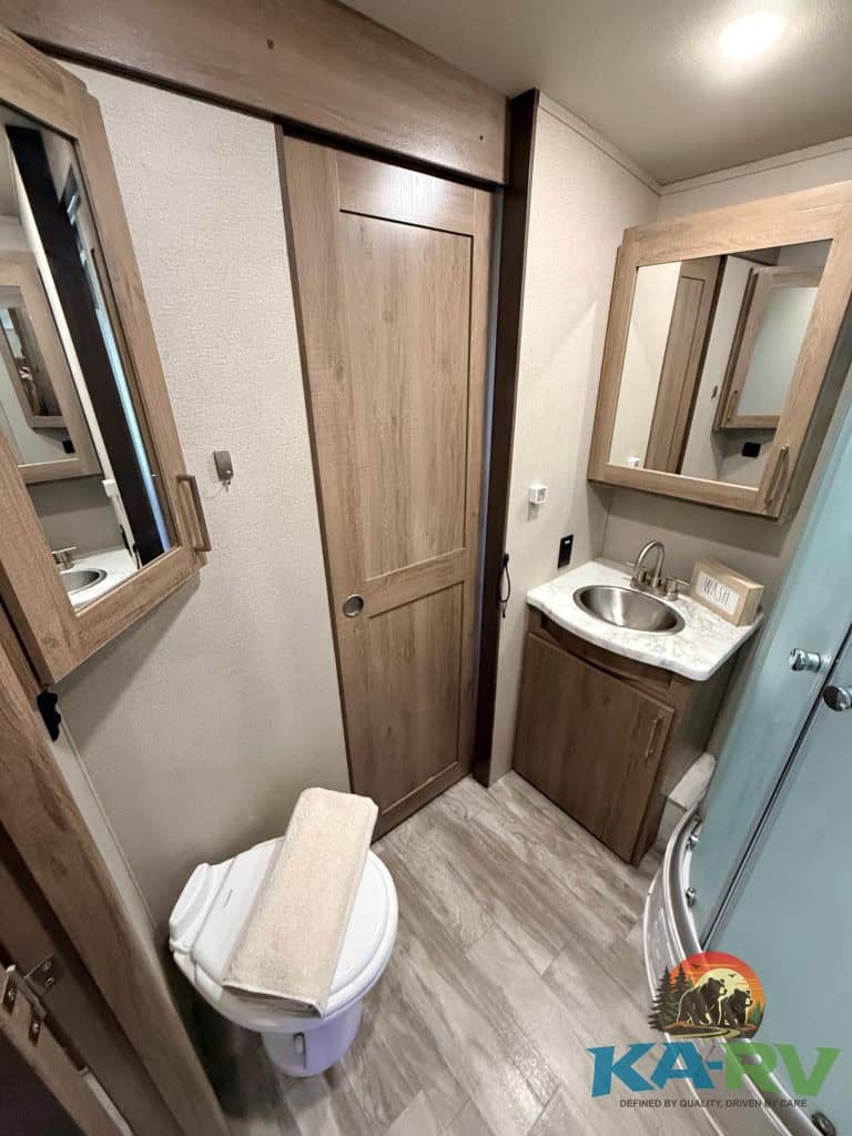 Efficient RV bathroom featuring wooden cabinets, a sink, and a shower for optimal space utilization.