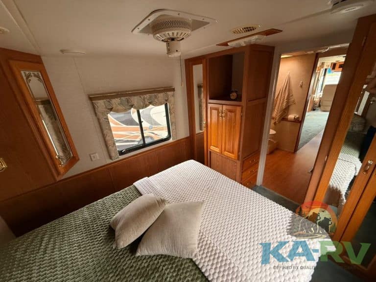 RV bedroom interior with cozy bed, wooden cabinets, and window view, ideal for comfort and relaxatio.