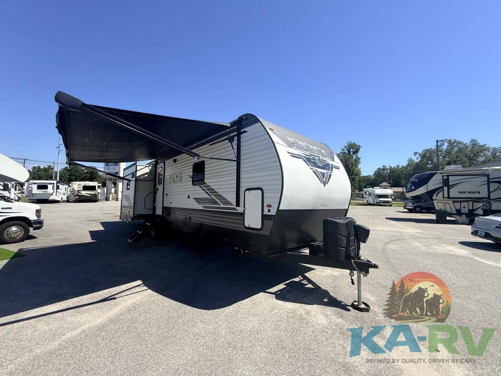 Modern travel trailer with awning at RV dealership lot.