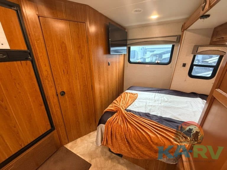 Cozy RV interior with bed, TV, and wooden cabinets for travel comfort.