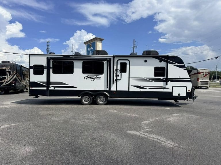 Modern travel trailer parked outdoors with blue sky and clouds.