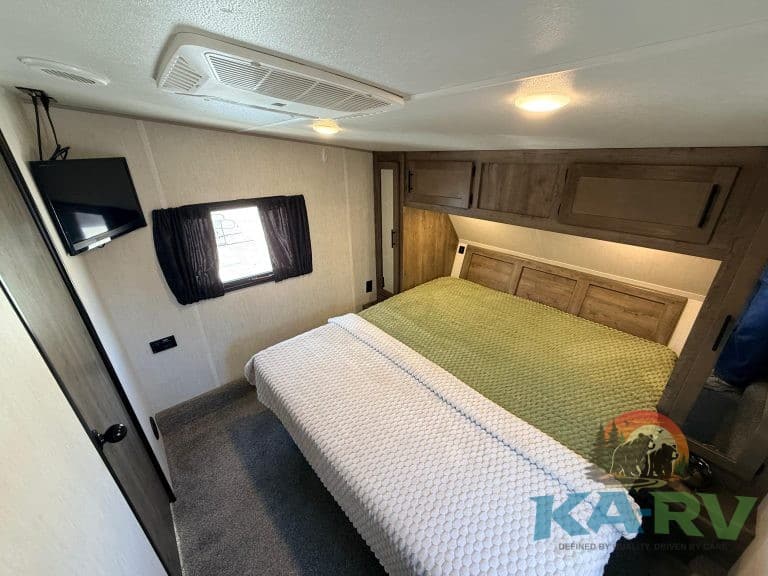 RV bedroom with cozy bed, wooden cabinets, and window for a relaxing camping experience.