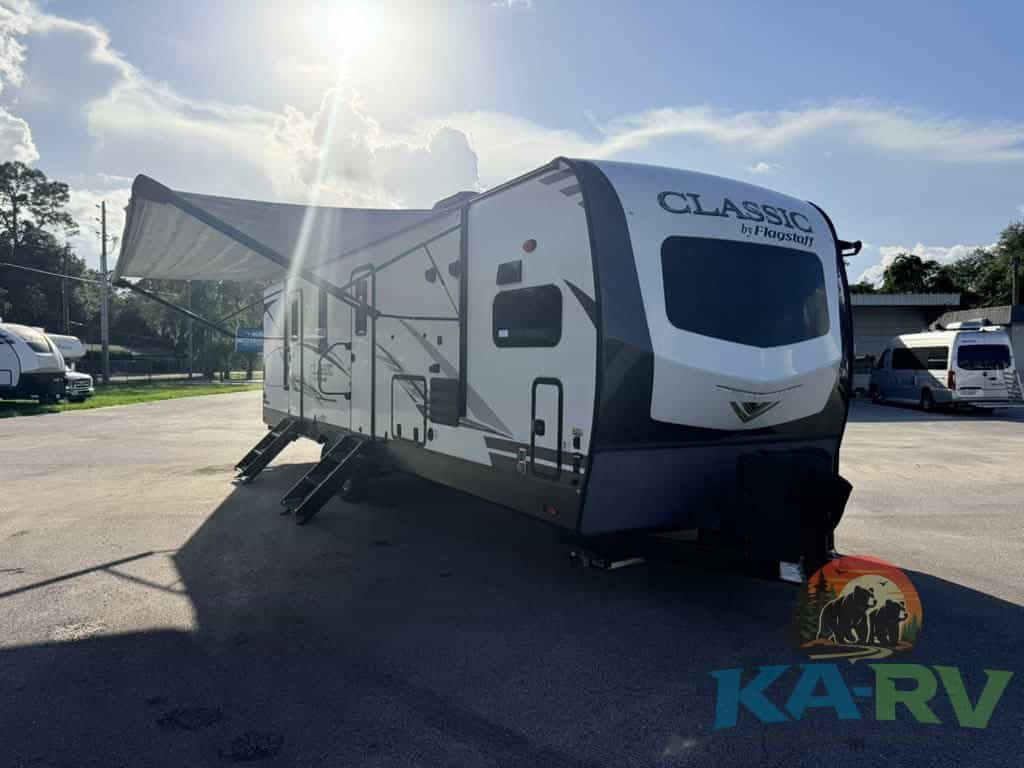 Travel trailer with awning extended at RV repair lot under sunny sky.