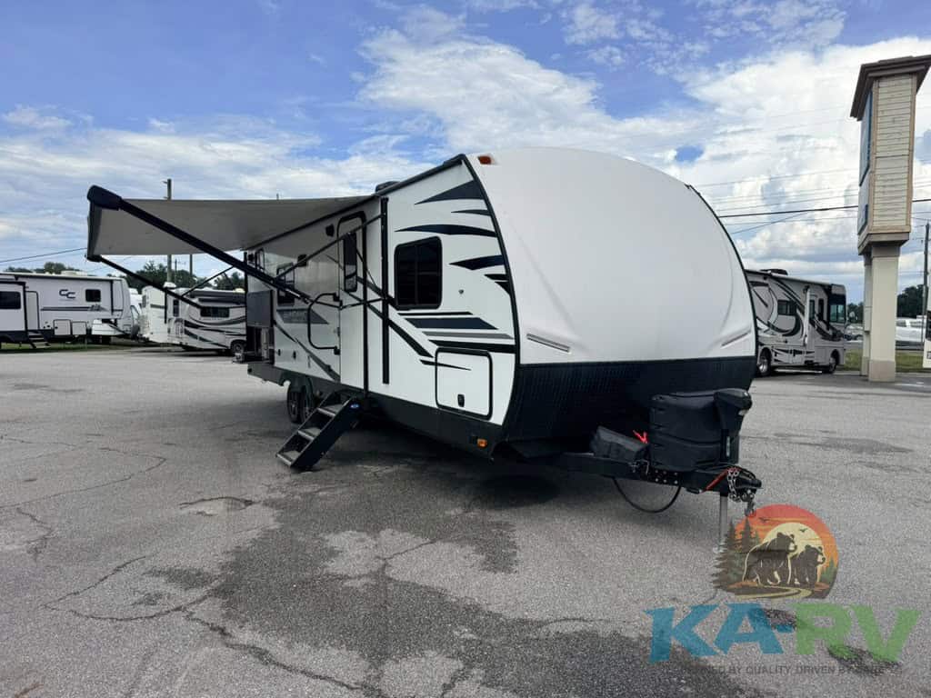 Travel trailer with awning at RV dealership, ready for camping trips.