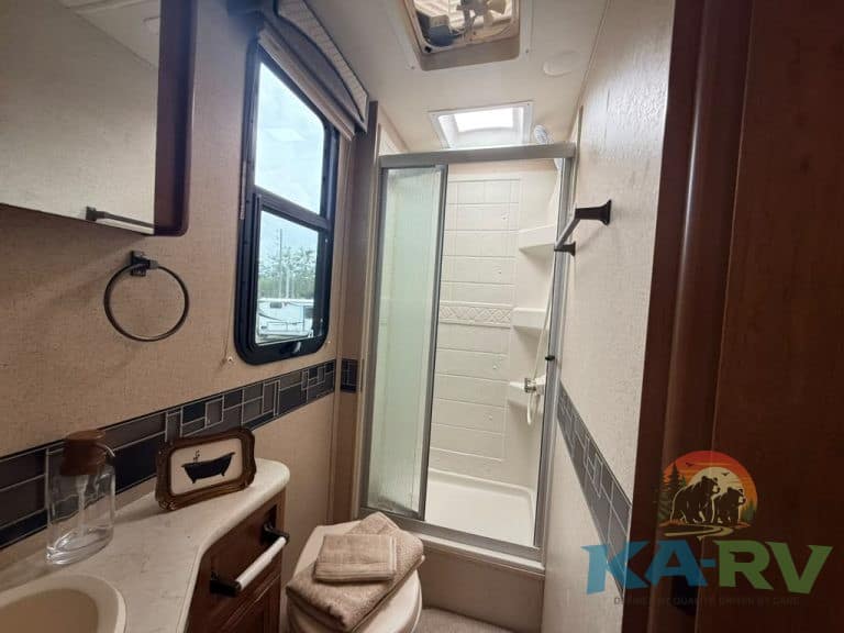 Small RV bathroom with shower, window, and storage space.