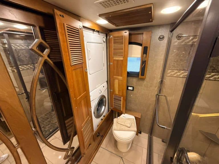 RV bathroom with washer and dryer, wooden cabinets, and shower stall.