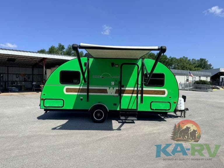 Green travel trailer with awning parked on lot under blue sky.