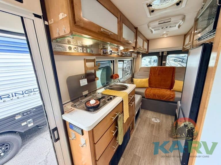 Cozy RV kitchen with stove, sink, and seating area.