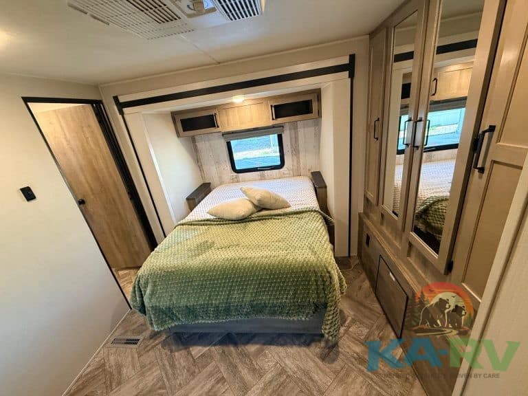 RV bedroom with storage cabinets, window, and cozy bed setup.