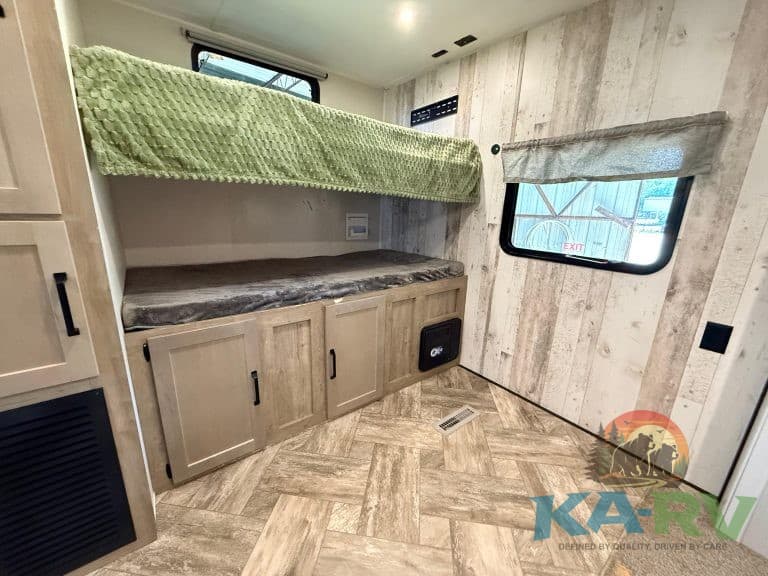 Interior view of RV bunk beds with storage cabinets and window.