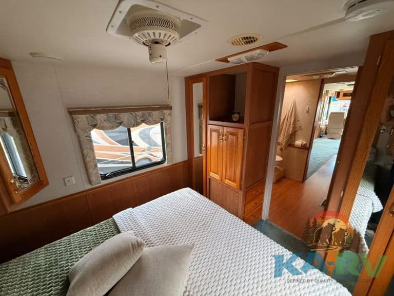 An inviting RV bedroom featuring wooden cabinets, a large bed, and natural light from a window.