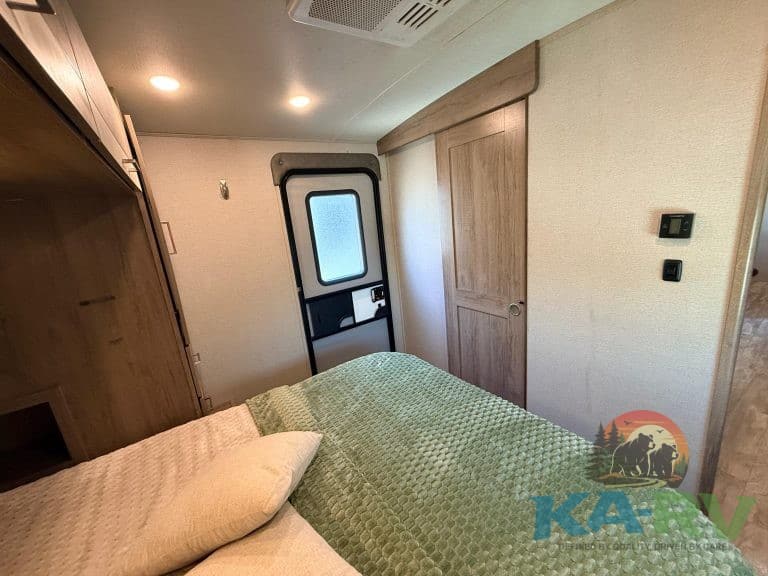 RV bedroom interior with wooden cabinets, bed, and door, showcasing a cozy and functional space for.