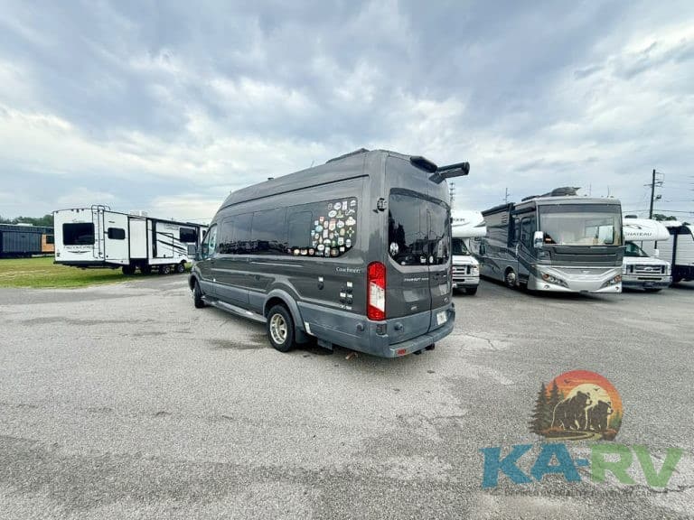 Black RV repair van parked in lot with other RVs and trailers under cloudy sky.