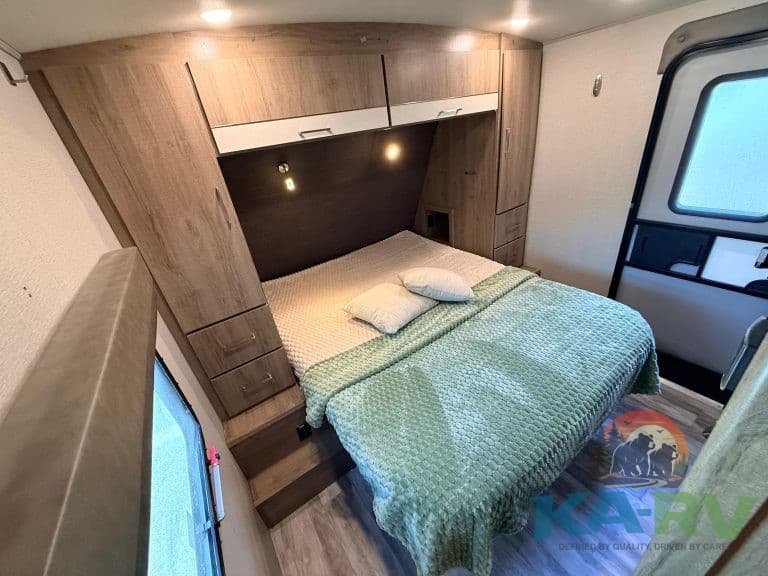 RV bedroom interior with cozy bed, wooden storage cabinets, and natural lighting. Perfect for comfor.