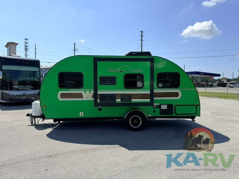 Green travel trailer parked outdoors with a clear sky and other RVs nearby.