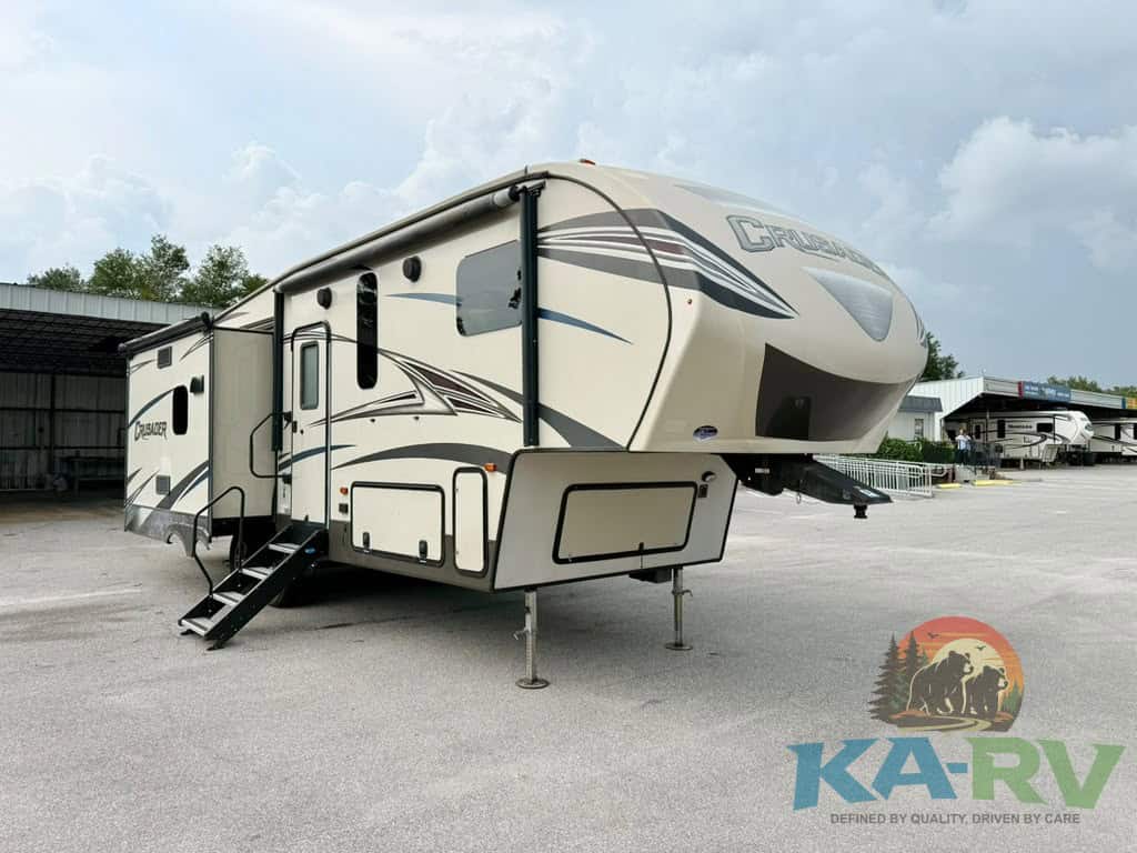 Modern beige fifth wheel RV with slide-outs and stairs at RV dealership.