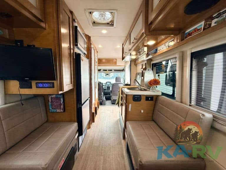 RV interior with seating, kitchen, and windows for travel comfort.