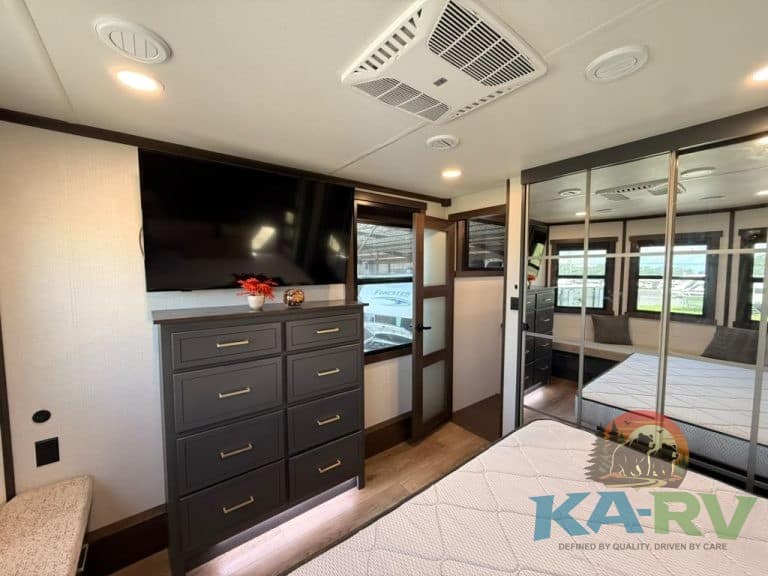 Modern RV interior with TV, dresser, and bedroom area.
