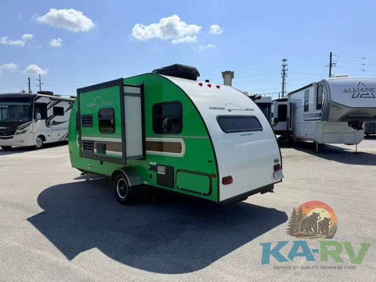 Green and white travel trailer with slide-out at RV dealership.