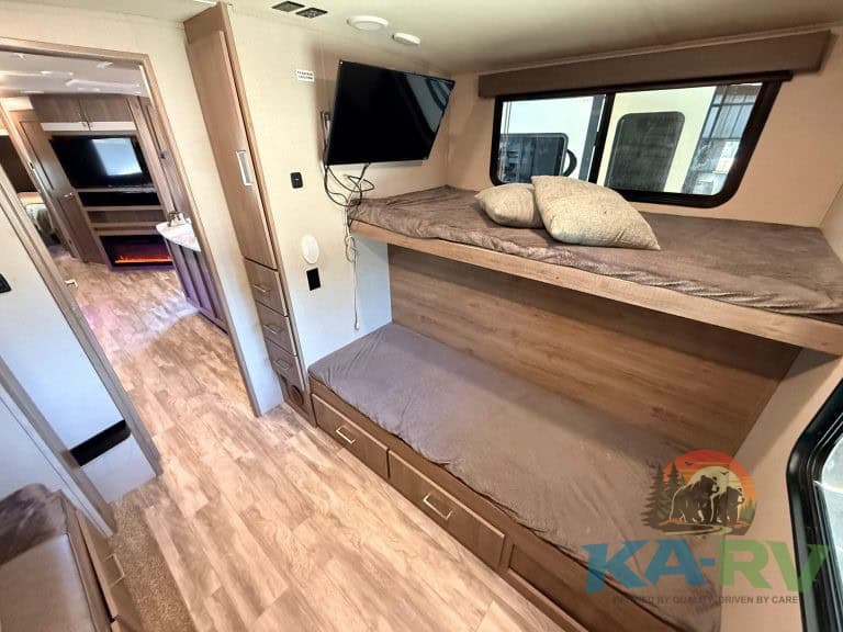 Bunk beds inside an RV with a mounted TV, cozy bedding, and wood accents.
