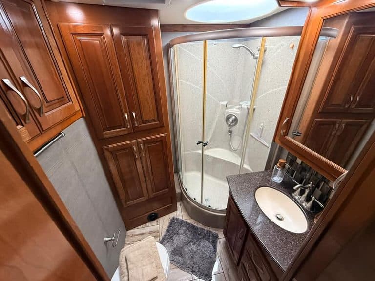 Luxury RV bathroom with shower, sink, and wooden cabinets.