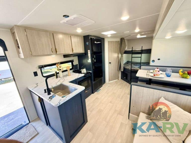 Modern RV interior with kitchen, sleeping area, and storage.