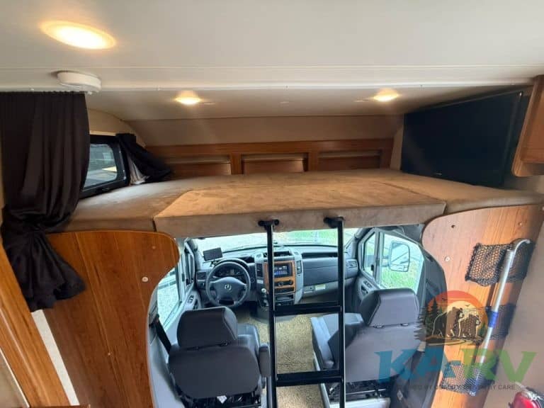 Overhead bed in RV with ladder and window view.