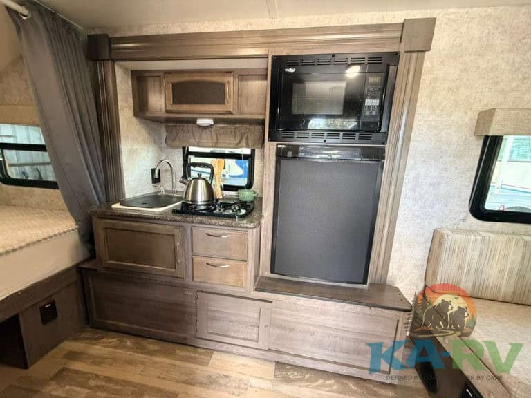 RV kitchen with microwave, refrigerator, and cabinetry in a Winnebago Winnie Drop.