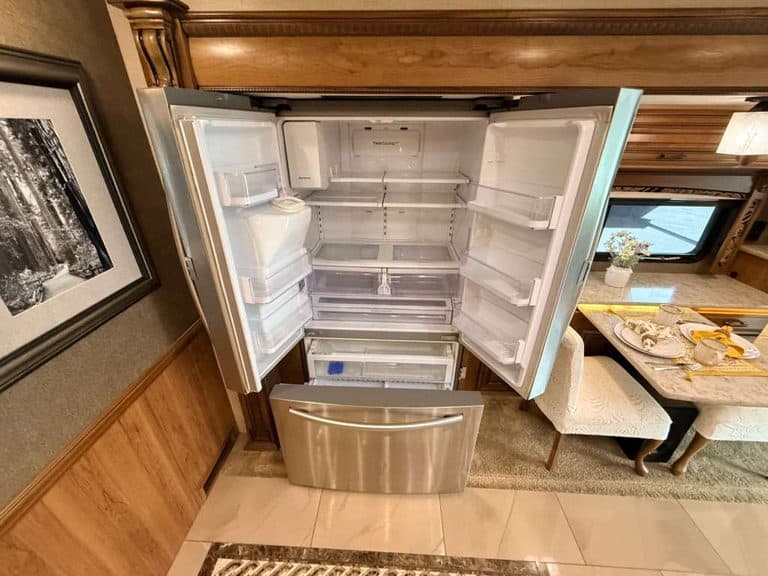 Open refrigerator in RV kitchen with empty shelves and drawers.