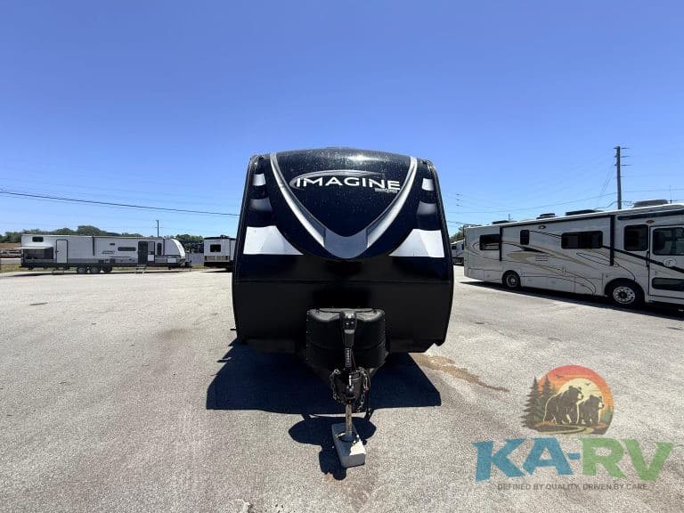 Travel trailer with "IMAGINE" branding, parked outdoors on a sunny day.