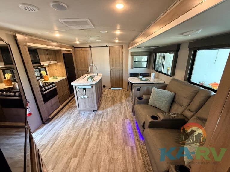 RV interior showcasing a compact kitchen and cozy living space with large windows and comfortable se.