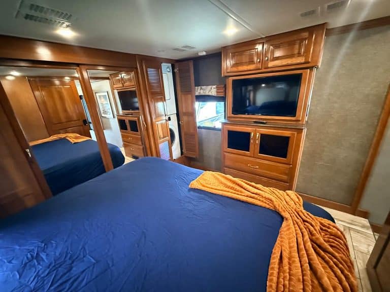 Luxury RV bedroom with wooden cabinets and a flat-screen TV.