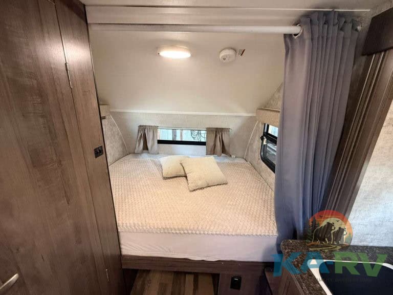 Cozy RV bedroom with bed, pillows, and window curtains in a 2017 Winnie Drop 1780.