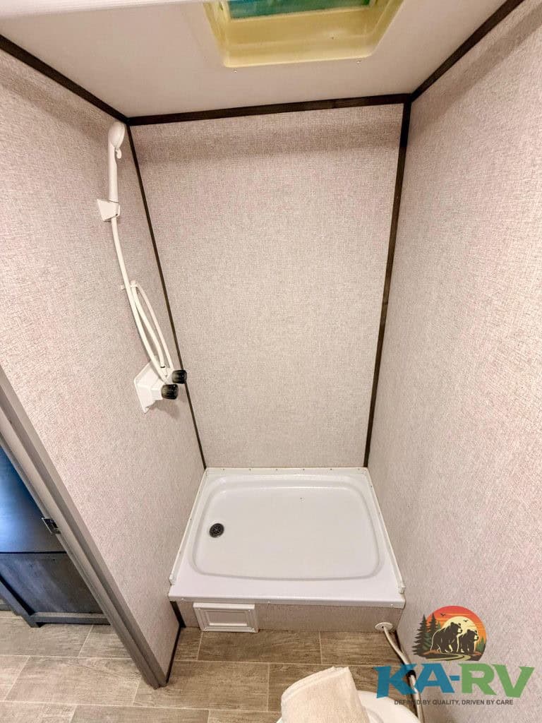 RV shower stall with beige walls, handheld showerhead, and skylight for natural light.