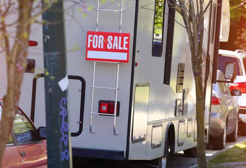 RV for sale with "For Sale" sign, parked on the street near trees and other vehicles.