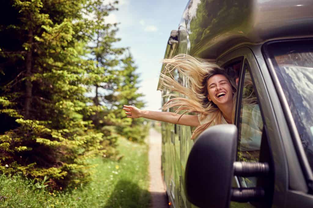 RV travel adventure with a smiling woman enjoying the outdoors from her RV window.