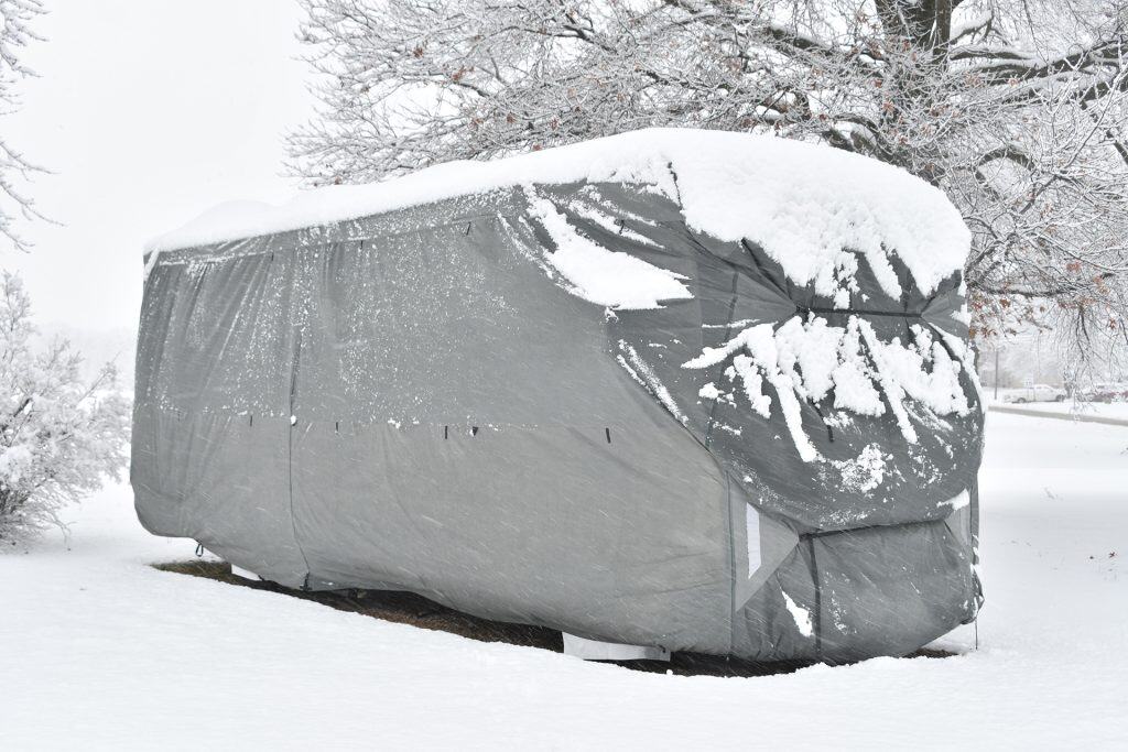 RV covered with a snow tarp in a snowy landscape.