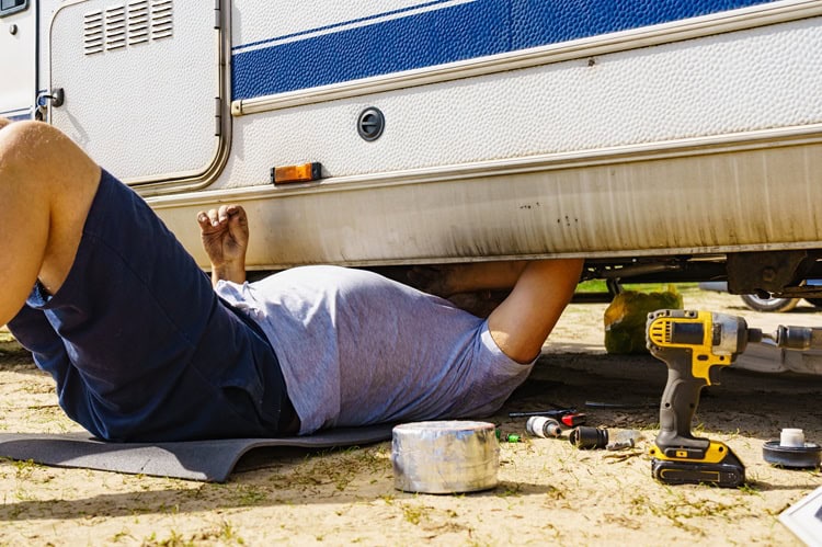Person repairing RV underside with tools, emphasizing proper RV maintenance.