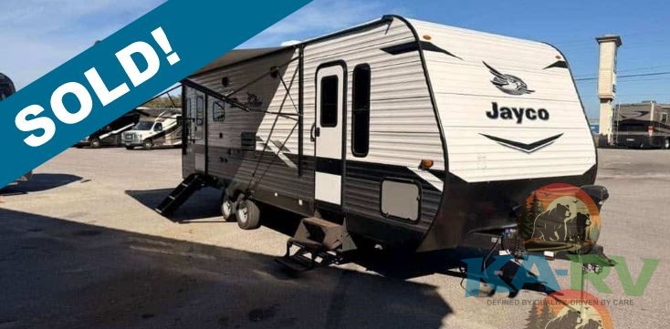 Travel trailer RV parked at dealership with 'SOLD' banner.
