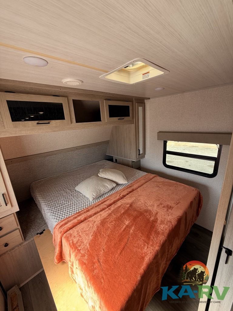 RV bedroom interior with cozy bed, overhead storage, and window views for optimal comfort.